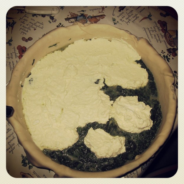 In einer mit flach ausgerolltem Teig überstehend ausgeschlagenen Springform wird Ricotta auf dem Spinat Spinat aufgebracht.