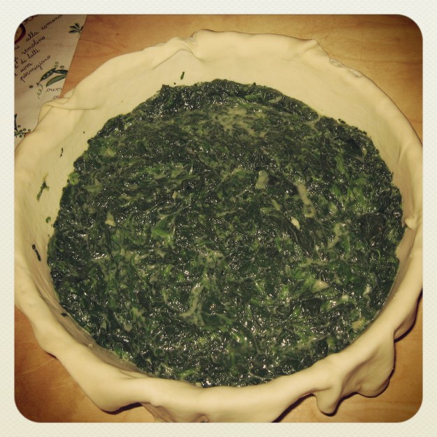 Die mit flach ausgerolltem Teig überstehend ausgeschlagene Springform wird mit Spinat gefüllt.