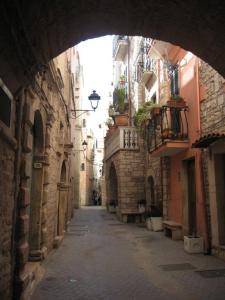 Von einem Bogengang aus fotografierte Altstadtstraße von Bitonto mit hohen Häusern aus hellen Steinen und schmalen Balkons.