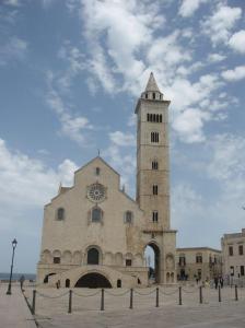 Die Frontansicht der Kathedrale von Trani zeigt den Treppenaufgang zum Portal, die große Fensterrose und den freistehenden GLockenturm direkt am Meer.