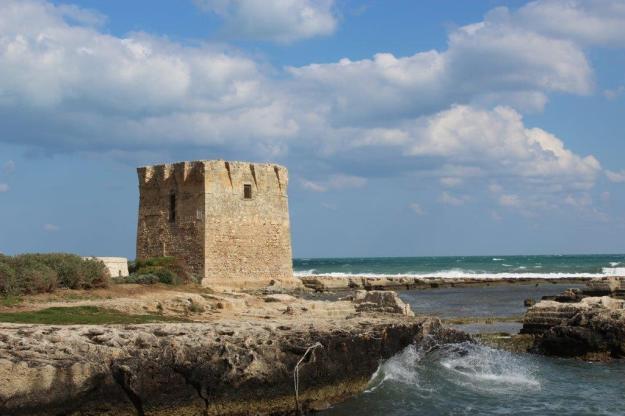 Auf schroffen Felsen steht der Normannische Küstenwachturm in San Vito bei Bari und wird von grünblauen Meer umspielt.