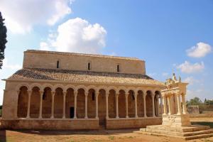Der romanische Bogengang vor der rotgoldenen Tuftsteinkirche der Abetei Santa Maria di Cerrate in der Nähe vonLecce bietet Besuchern ein schattiges Pätchen.