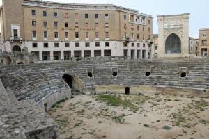 Ruinen des Amphitheaters in Lecce, dahiner ragen möderne Gebäude aus der Neuzeit auf.