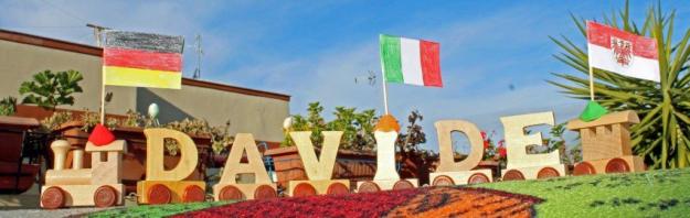 Ein Holzzug bestehend aus den Buchstaben des Namens Davide mit der italienischen, der deutschen und der Brandenburgflagge steht auf einem Tisch vor blauem Himmel.
