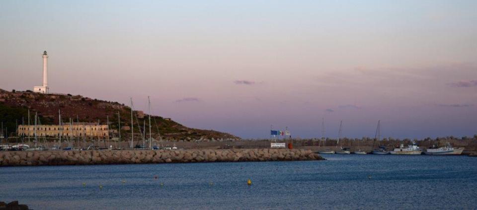 Die untergehende Sonne wirft ihre Letzten Straßen auf den Hafen und den Leuchtturm von Santa Maria di Leuca in Apulien.