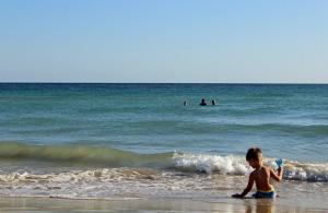 Ein Kind sind mit Buddelschippe am Strand der Malediven des Salento und vom blauen Meer kommen Wellen herangerollt. 