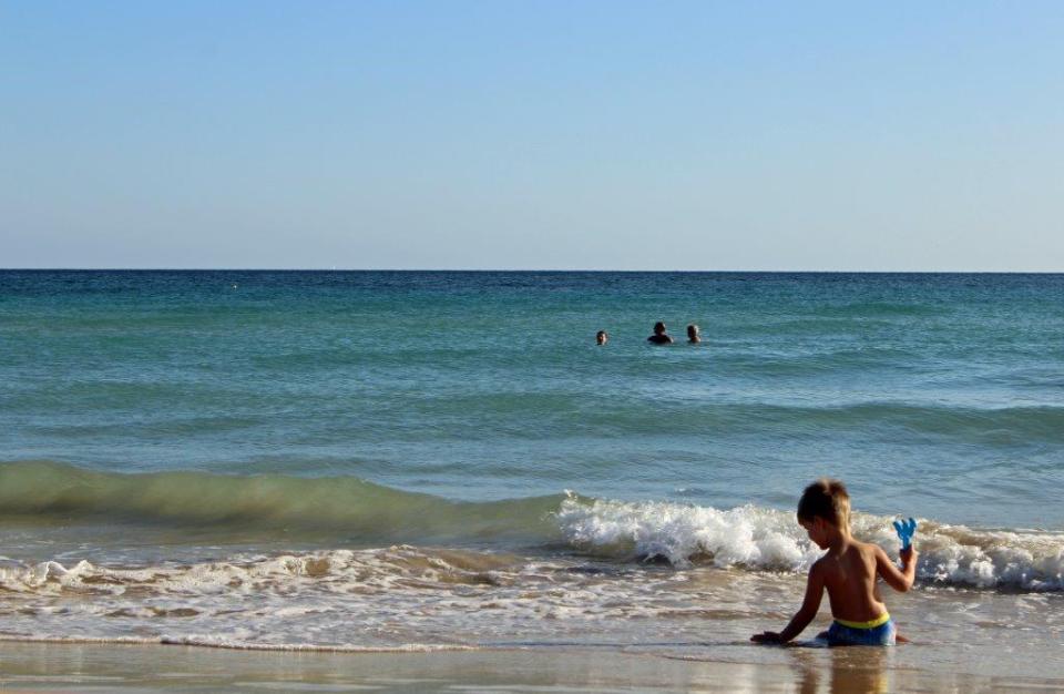 Ein kleines Kind platscht vergnügt im flachen Wasser am Strand sitzend und spielt mit den Wellen des Meeres.