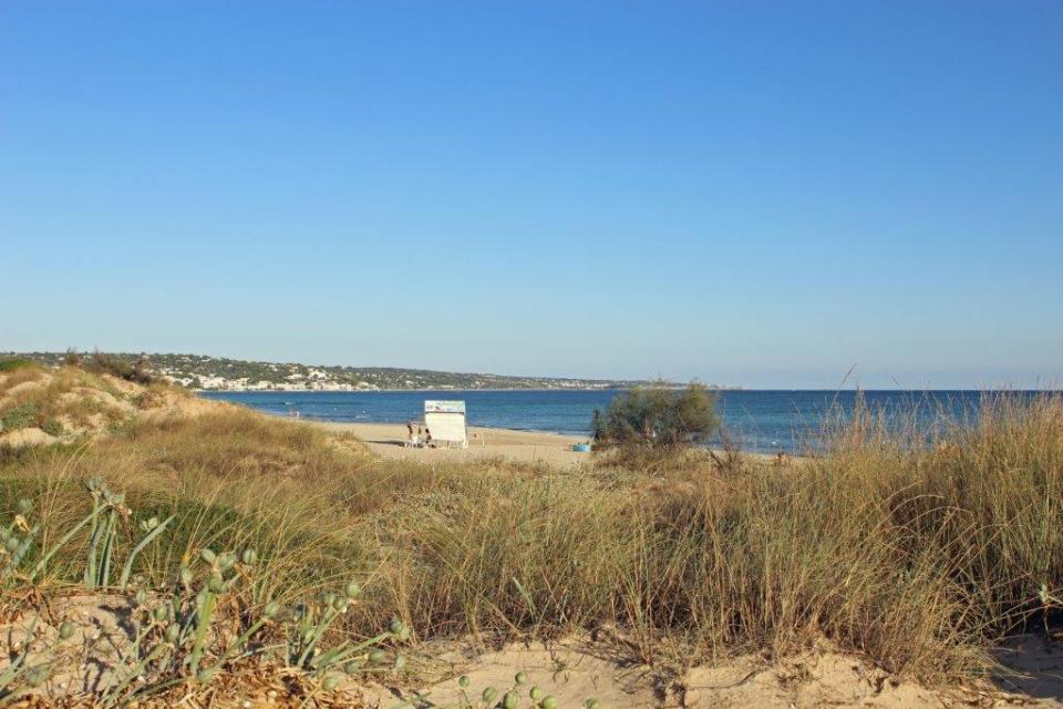 Der Blick über die Dünen des Strandes Maledive del Salento bei Santa Maria di Leuca in Apulien eröffnet einen Blick auf blaues Wasser und goldenen Sandstrand.