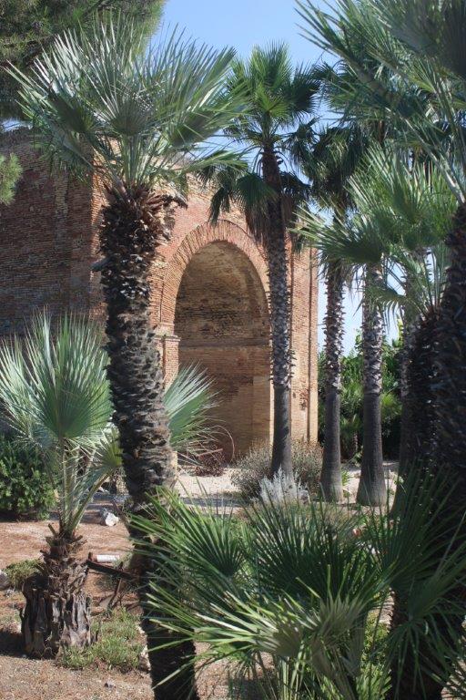 Inmitten der Ausstellungsfläche eines Gartenbaubetriebs erhebt sich der Torbogen Archo Varrone Archo Varrese auch Archo Traiano genannt, in Canosa hinter Palmen.