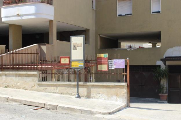 Von außen ist das Ipogeo Scocchera B-1 ein unscheinbarer Eingang in die Garage eines mehrstöckigen Mehrfamilienhauses. Davor weißt ein Schild auf die historische Stätte hin.