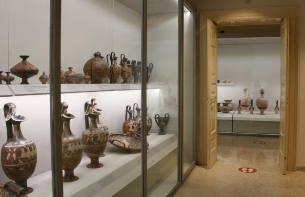 Eine massive Holztür gibt den Blick von einem ausstellungsraum in einen anderen frei im Archäologiemuseum Museo Archeologico Nazionale in Canosa, Apulien. Links eine Vitrine mit antiken Vase, die mit Szenen aus der Mythologie bemalt wurden.