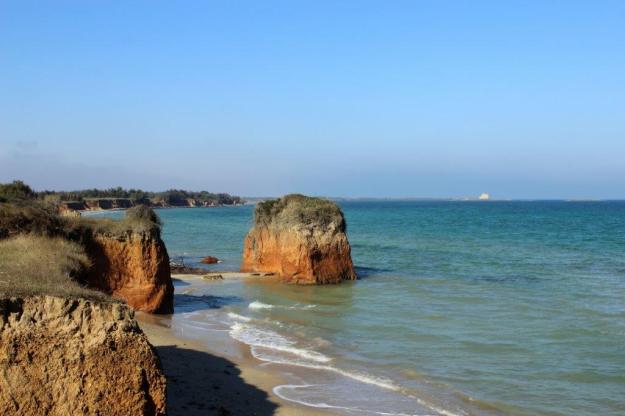 Rötliche Felsformationen ragen aus dem flaschen Meer am Strand von Torre Guaceto, Apulien,