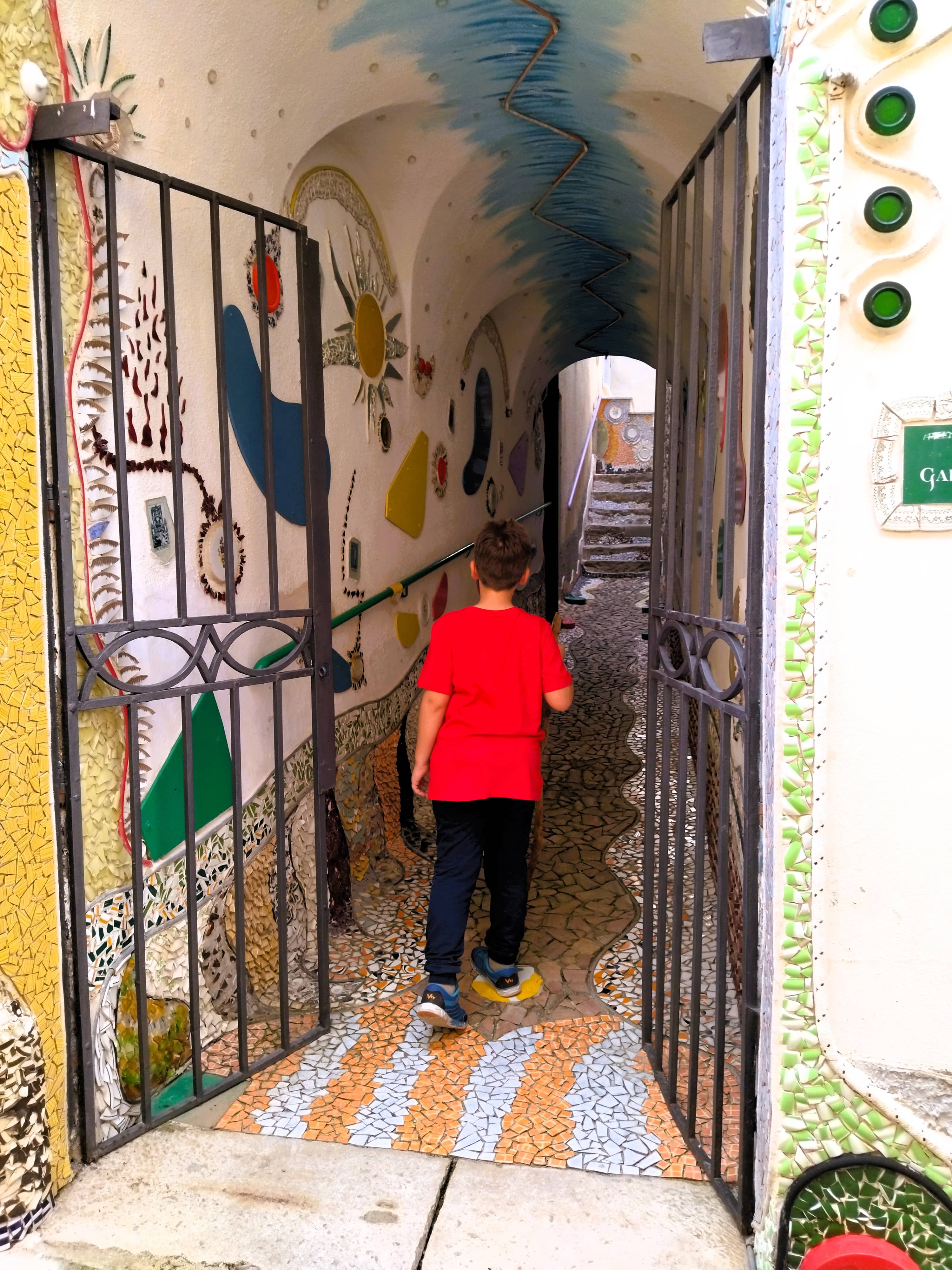 Kind betritt einen Häusertunnel, Hauswand und Straße mit Mosaiken aus Scherben von altem Geschirr, Forenza, Basilikata, Süditalien, Street Art
