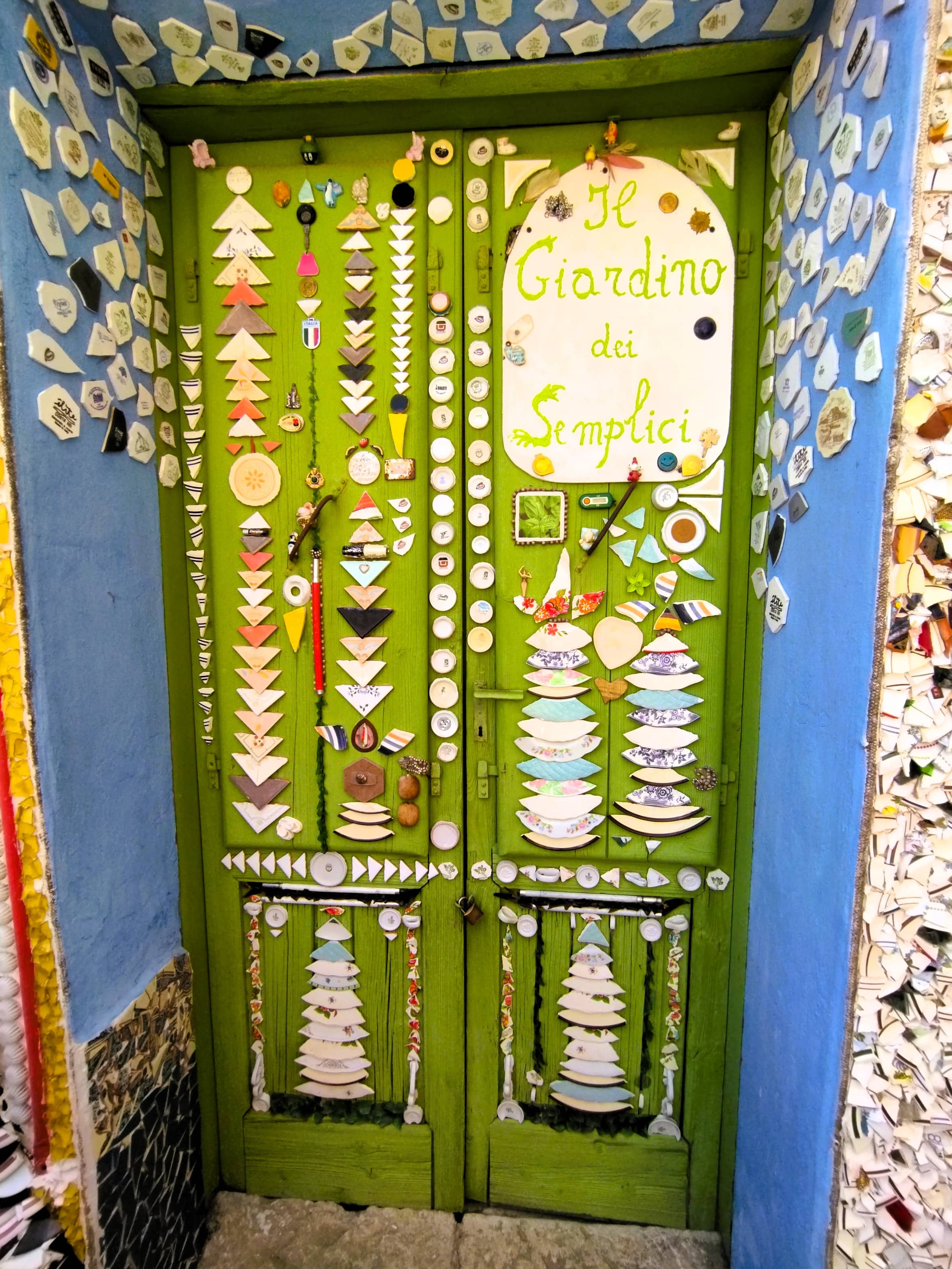 Hauswand und Tür mit Mosaiken aus Scherben von altem Geschirr und Aufschrift il giardino dei semplici, Forenza, Basilikata, Süditalien, Street Art