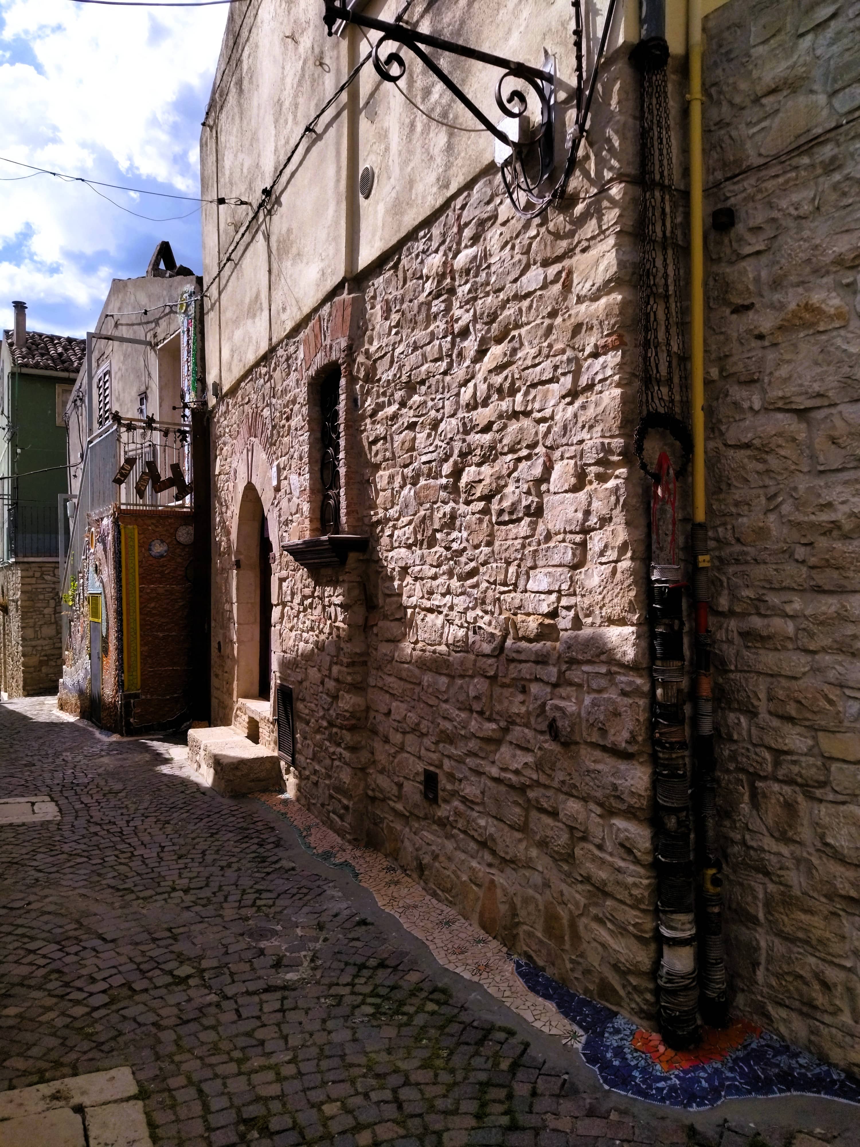 Straße mit Mosaiken aus Scherben von altem Geschirr auf dem Boden entlang der Hauswand, Forenza, Basilikata, Süditalien