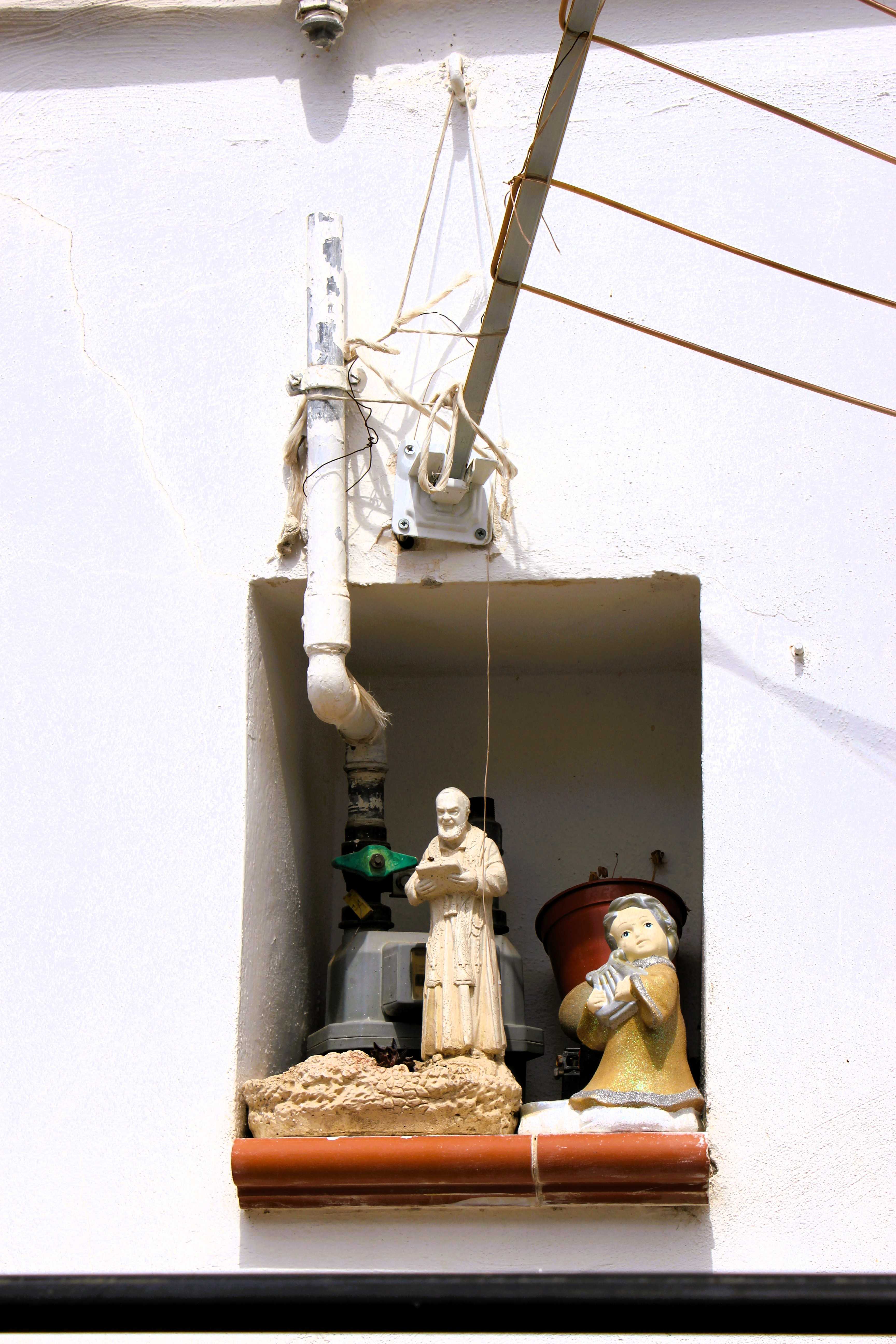In Policoro, Basilikata, wird eine Nische, die eigentlich für die Wasseruhr gedacht war, mit einer Statue von Padre Pio, einem Engel und einer Topfpflanze in einen Heiligenschrein umfunktioniert.