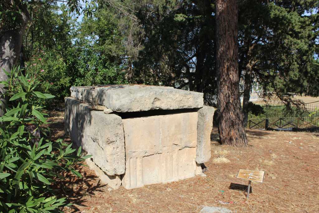 Vor den Archäologische Nationalmuseum Siritide in Policoro, Basilikata, steht ein steinerner Sarg, dessen Grabbeigaben sich jetzt im Museum befinden, unter Pinien.