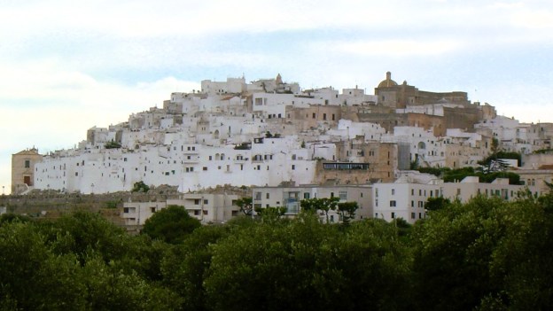Über Olivenbäumen erhebt sich auf einem Hügel die weiße Stadt Ostuni in den Himmel.