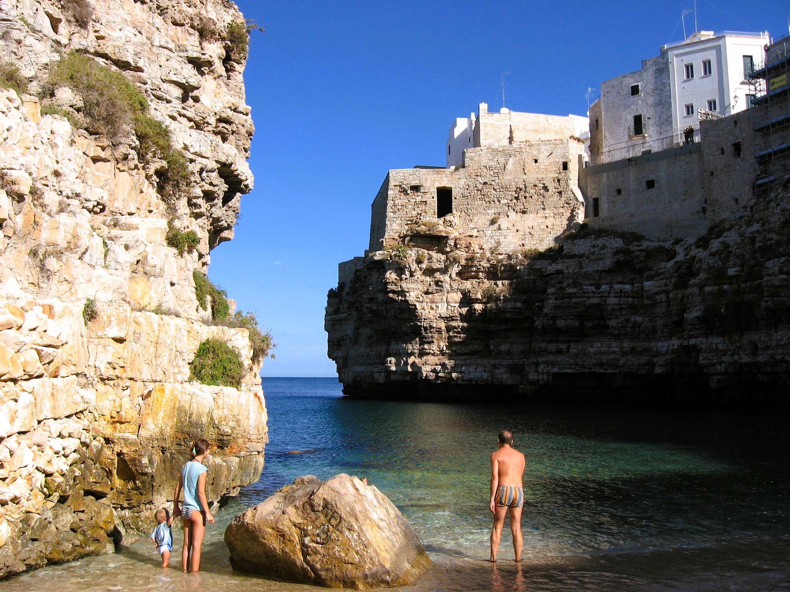 Zwischen zwei Klippen liegt der Stadtstrand von Polignano a Mare mit klarem Wasser und drei Badegästen im November.