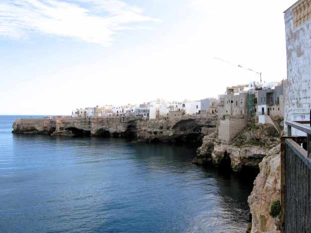 Von einem Aussichtsbalkon fotografierte Klippen von Polignano a Mare zeit die Eingänge der Meeresgrotten und die Häuser der Altstadt, die dicht an die Klippen herangebaut worden sind.
