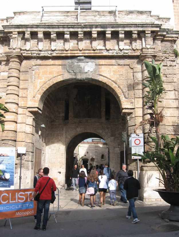 Durch ein goldgelbes Sandsteintor betreten Touristen die Altstadt von Polignano a Mare in Apilien.