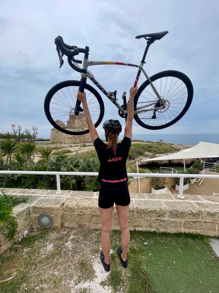 Radfahrer reckt begeistert sein Bike in die Höhe wöhrend er auf Olivenbäume und das Meer von Apulien schaut.