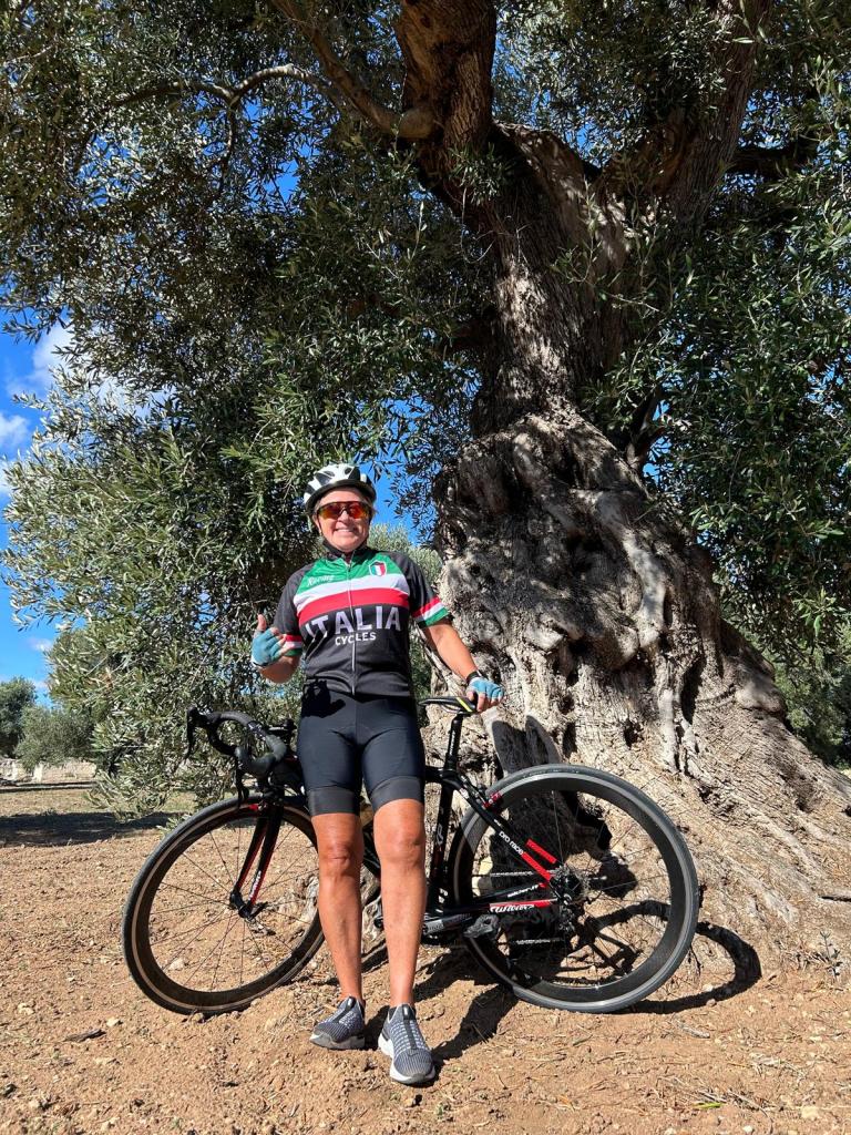 Radfahrer mit seinem Fahrrad vor einem jahrhunderte alten Olivenbaum im Apulien.